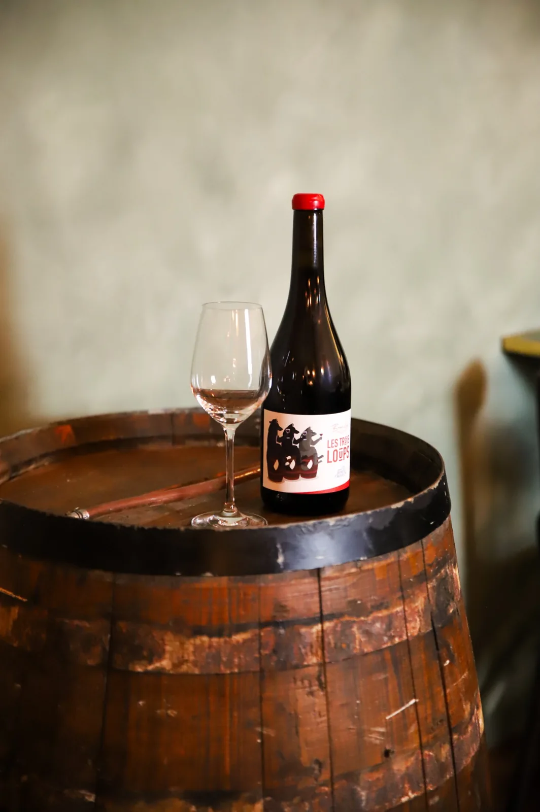 Botella de vino natural y copa sobre una barrica